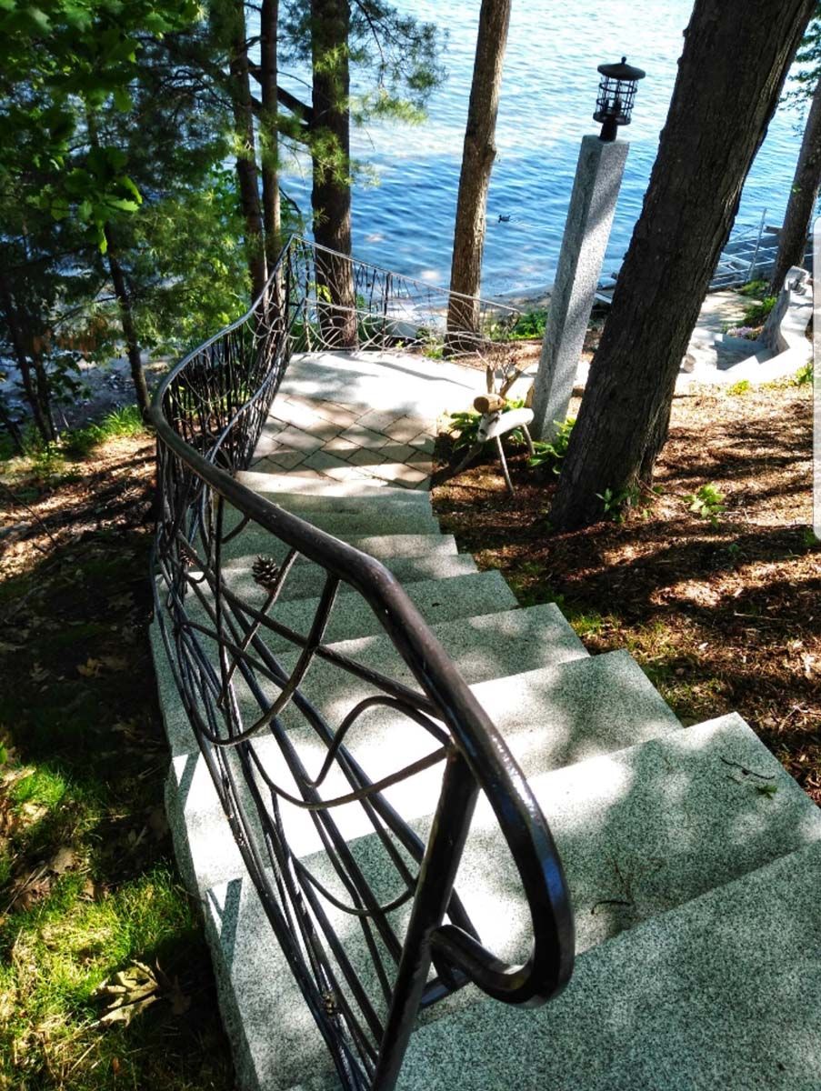 Stone staircase with decorative black railing leading to a lake.