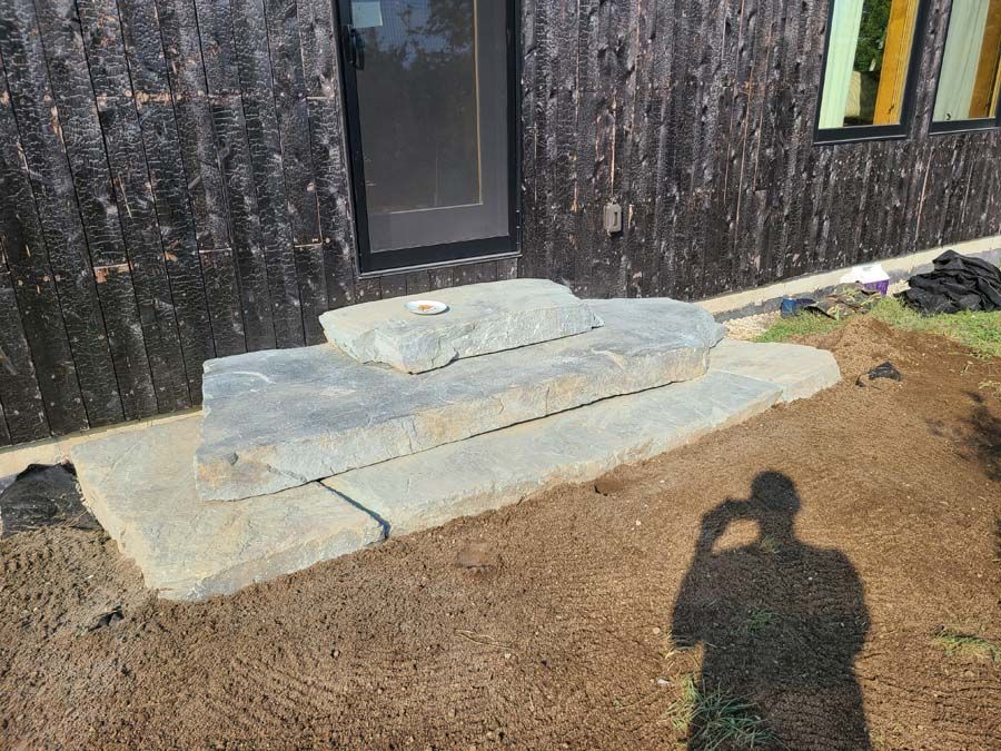 Stone steps leading up to a dark-walled building. Shadow of a person taking a photo.