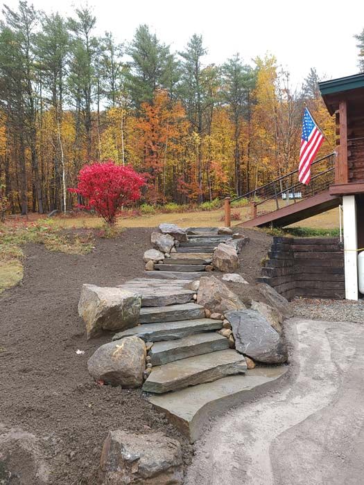 Stone steps leading up a hill with colorful fall trees in the background; American flag on a porch.