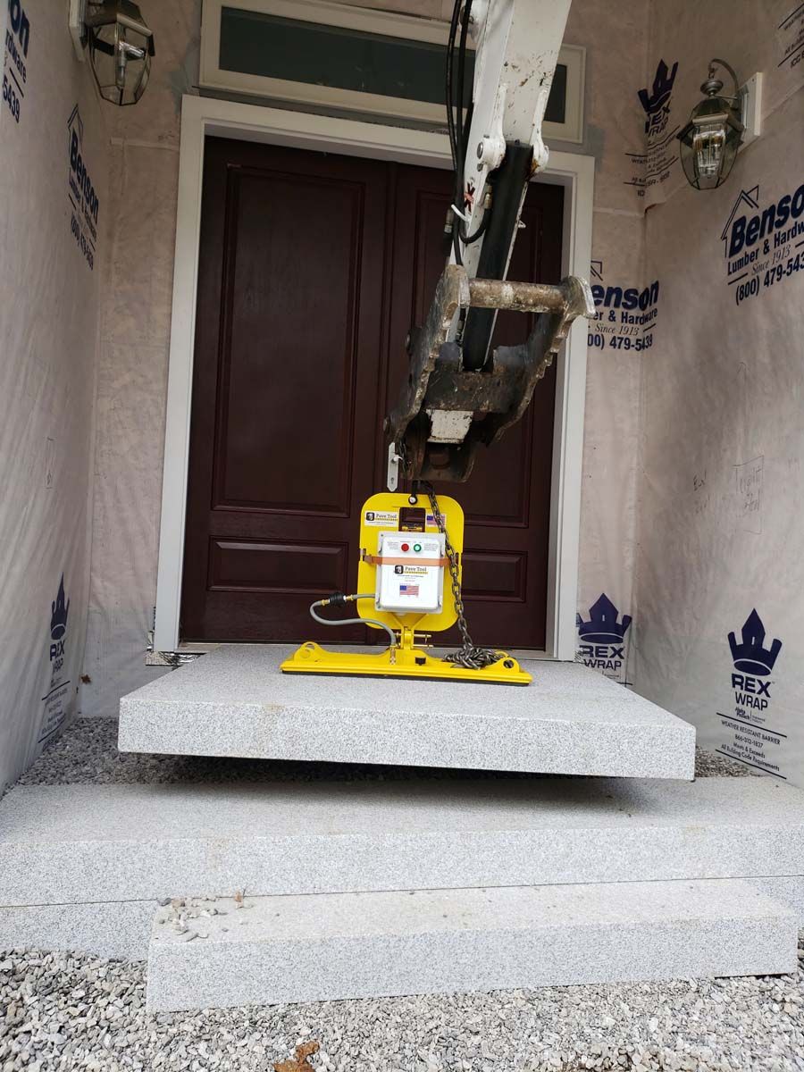 A machine lifts a granite step onto a porch near a brown door. Construction in progress.
