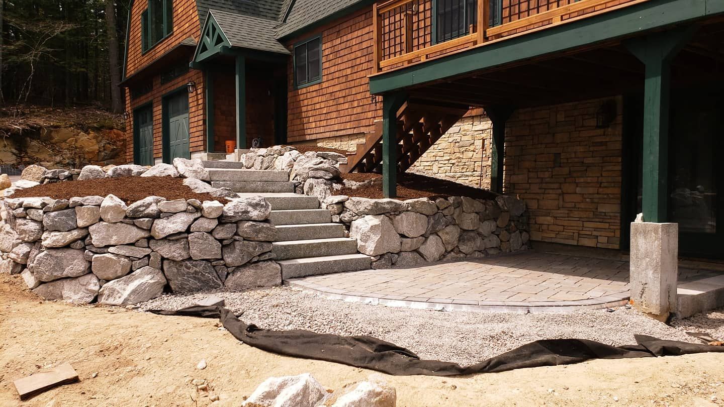 Stone steps and retaining wall leading up to a brick house with a covered patio.