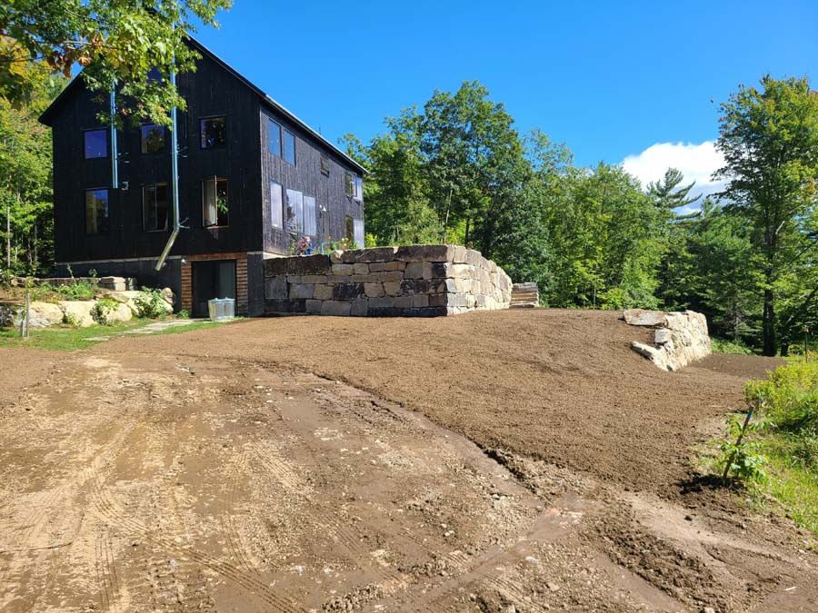 Black house with stone foundation on a sunny day. Brown dirt grading.