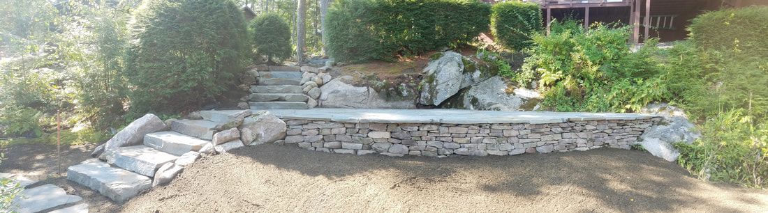 Stone steps leading up to a raised garden bed, surrounded by greenery and lawn.