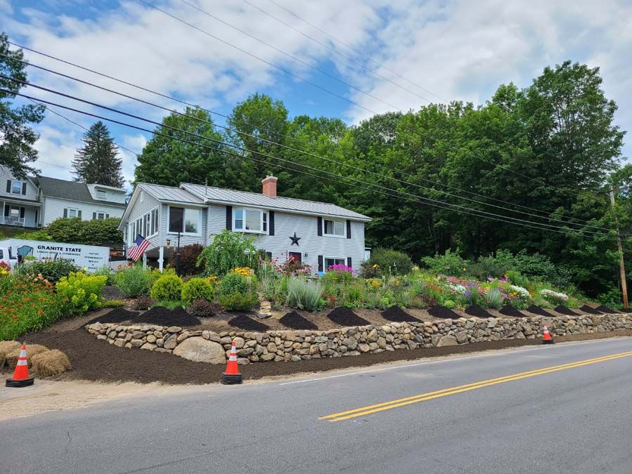 A house with a stone wall, a colorful garden, and a blue sky.