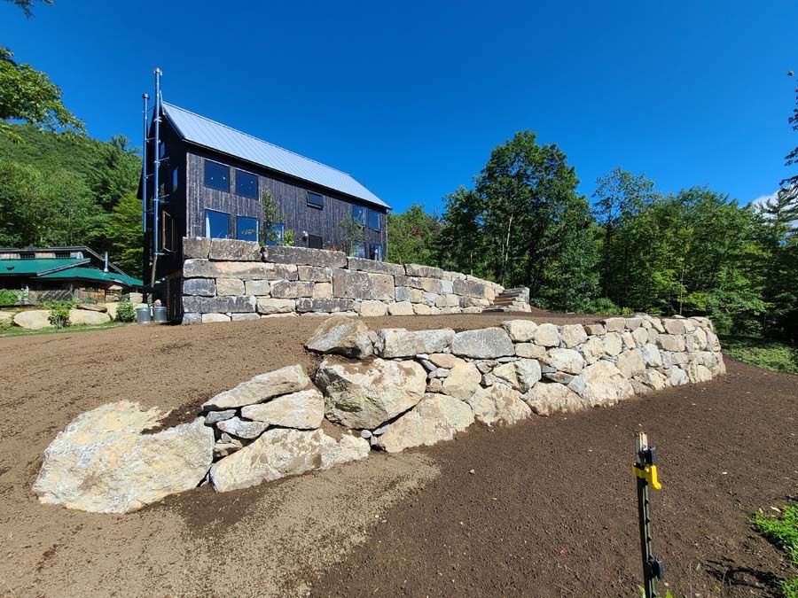A dark-stained house with a stone retaining wall on a sunny day.