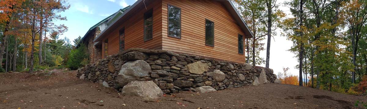 A log cabin on a rocky foundation sits among autumn trees.