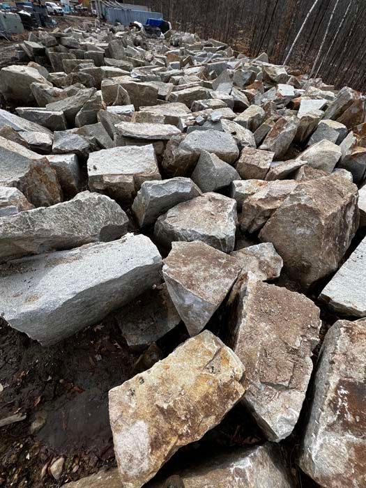 Pile of rough-cut gray and brown stones, likely for construction, outdoors.