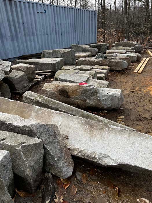 Gray stone blocks and slabs piled outdoors near a blue shipping container.