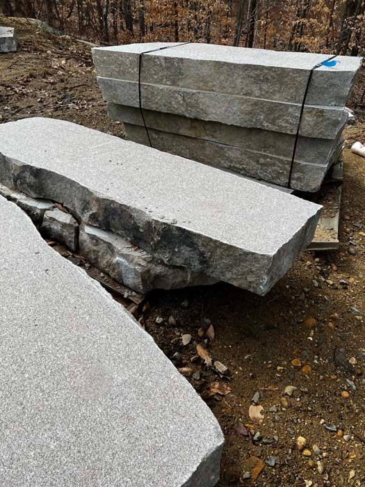 Gray stone slabs stacked and lying on the ground, likely for construction.