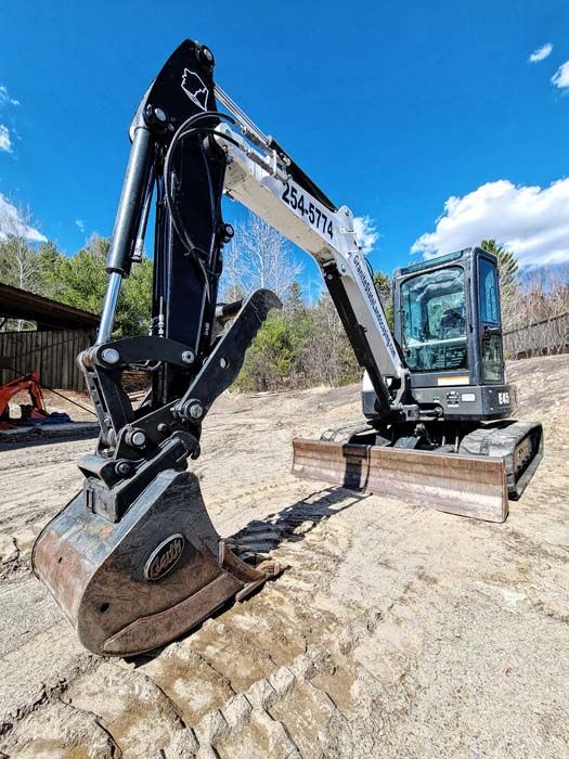 Black and white Bobcat excavator on a worksite under a blue sky.
