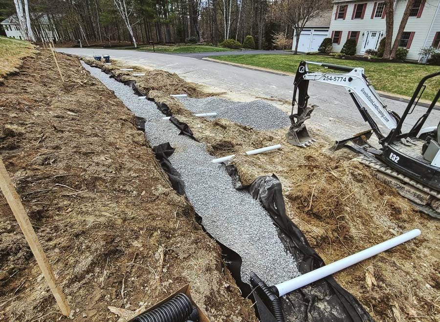 Construction of a drainage system in a residential area. A trench filled with gravel, pipes, and a small excavator.