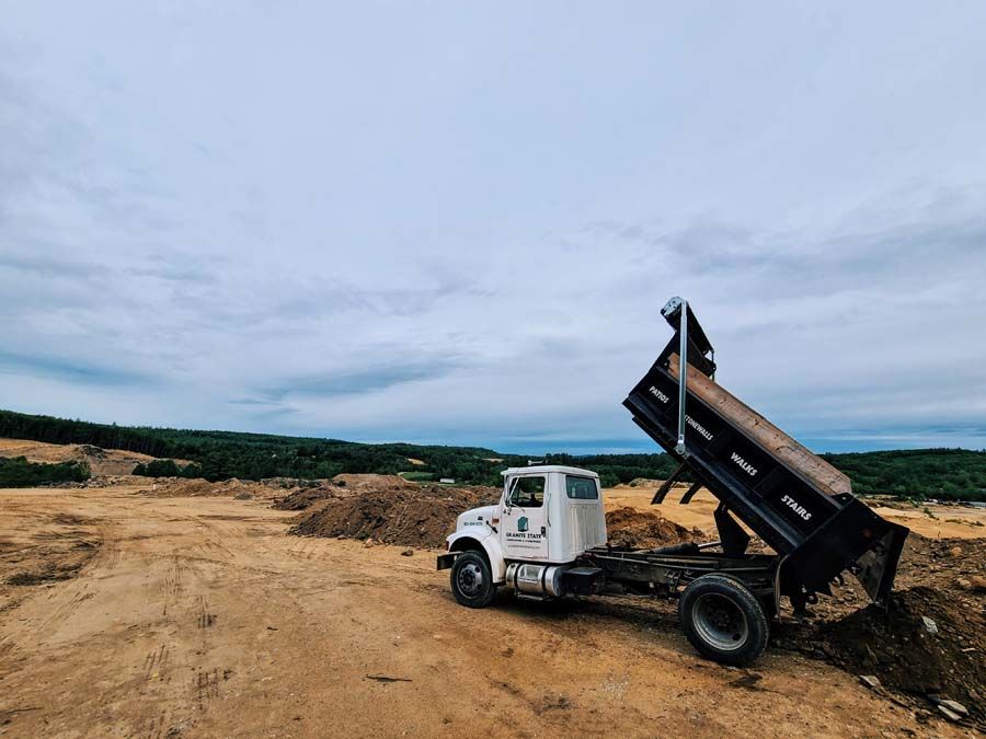 Dump truck, bed raised, in dirt field, overcast sky.