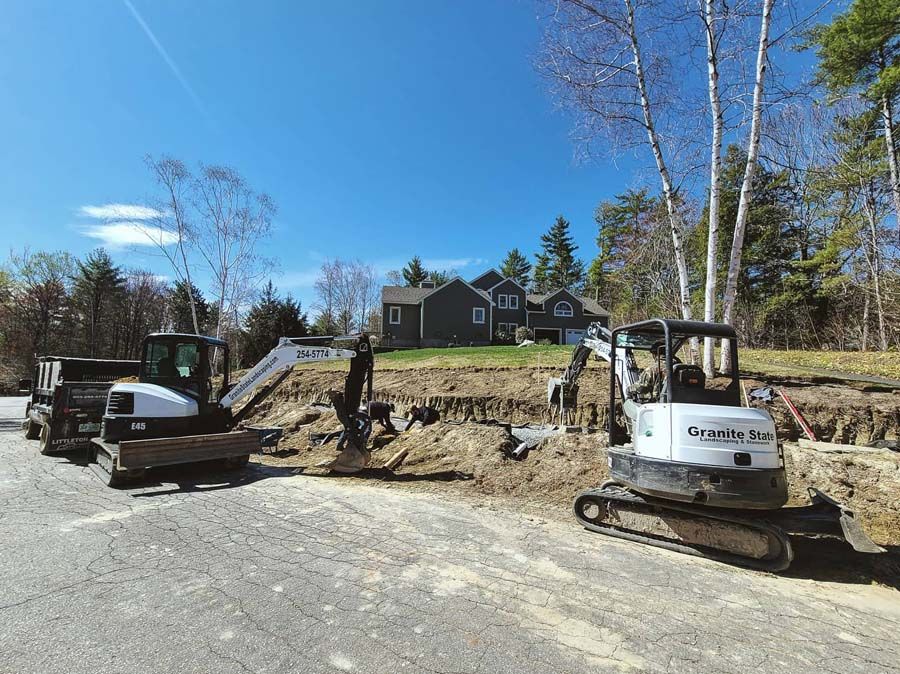 Two excavators and a dump truck at a construction site in front of a house. Blue sky.