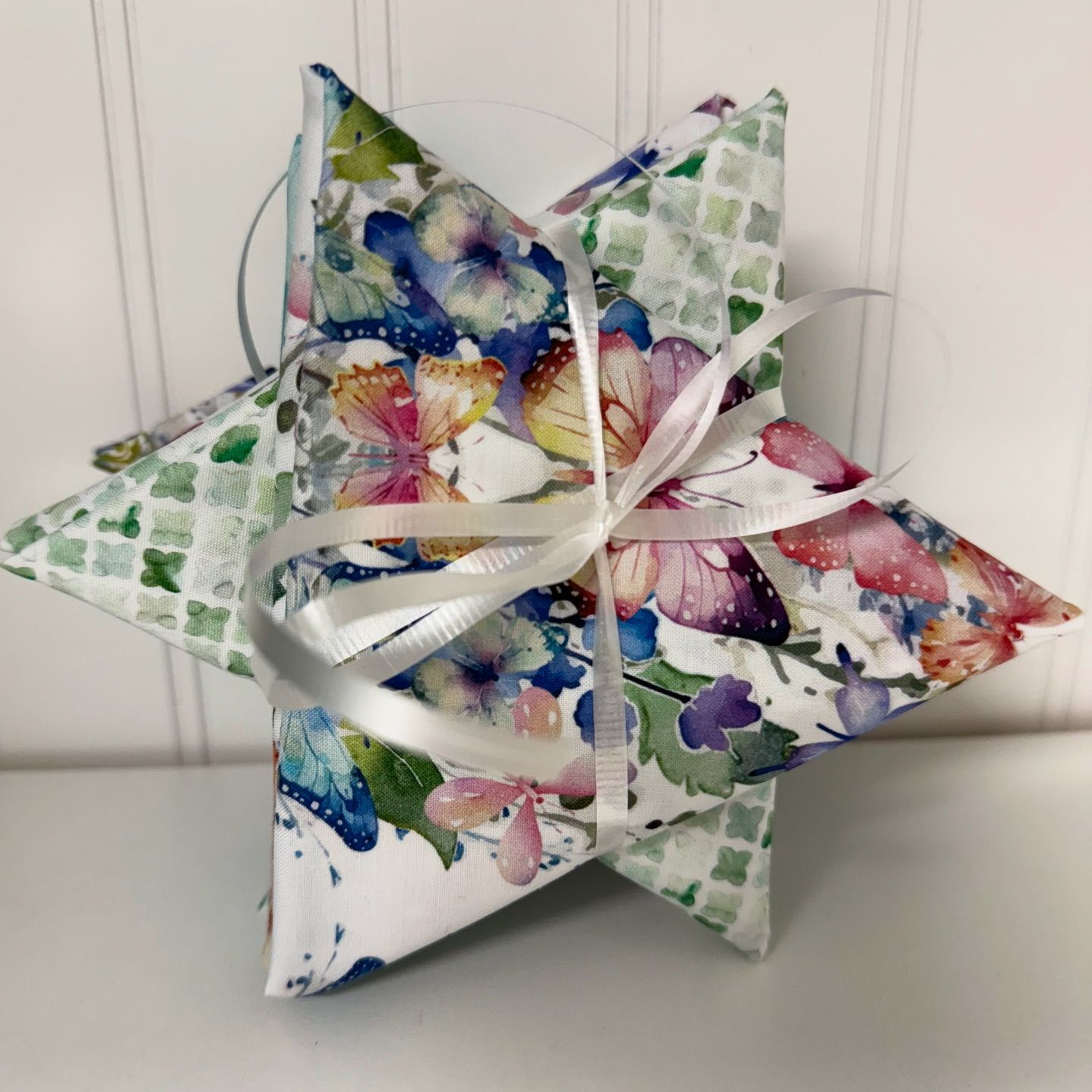 A star-shaped fabric ornament with a butterfly and floral print, tied with a white ribbon.