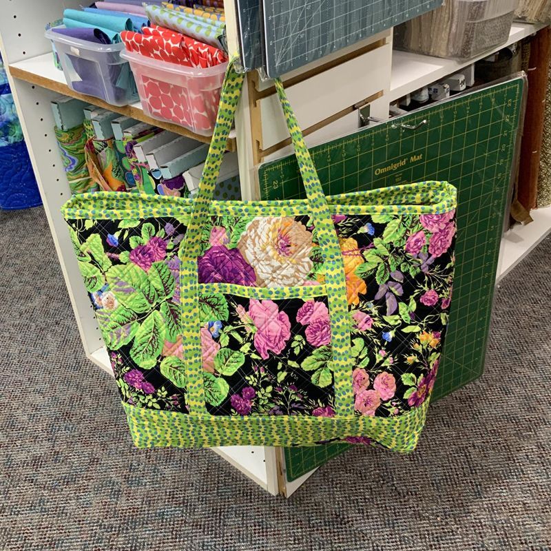 Tote bag with floral print and neon green trim, hanging in a fabric store.