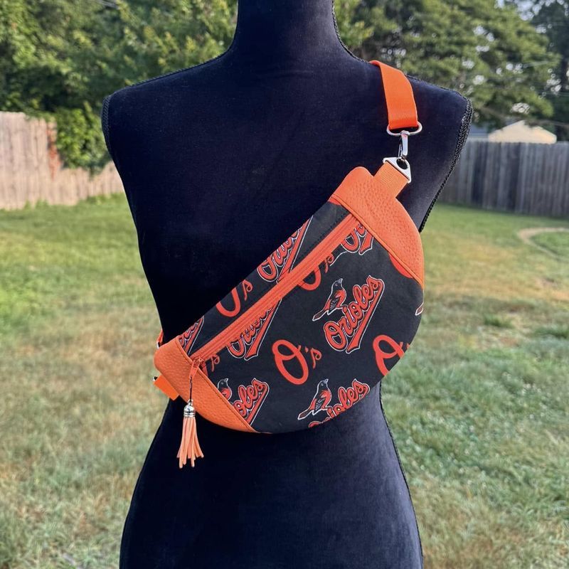 Black mannequin wearing an orange and black Orioles fanny pack outdoors.