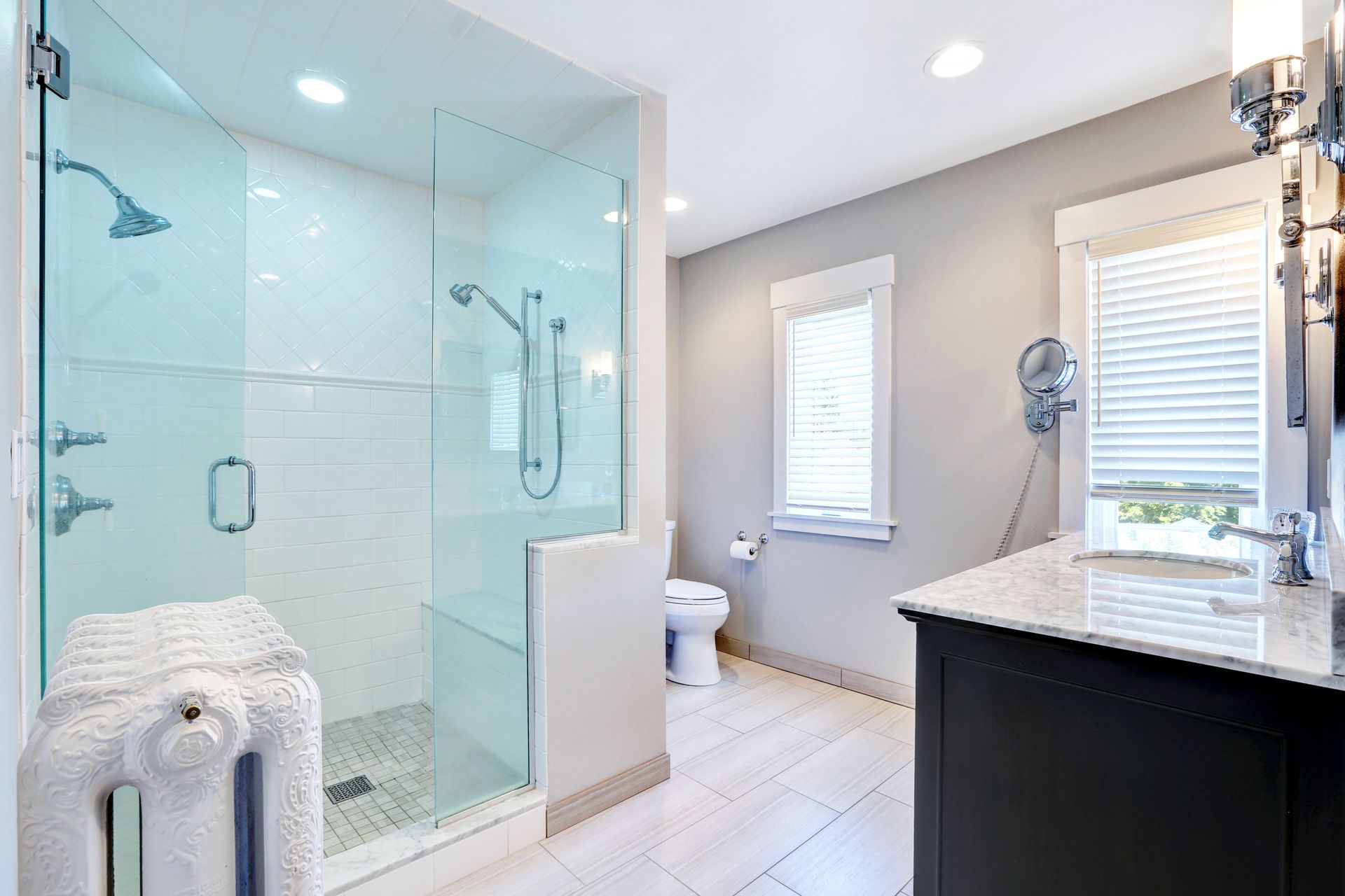 Modern bathroom: Glass shower, white walls, dark vanity, and white blinds.