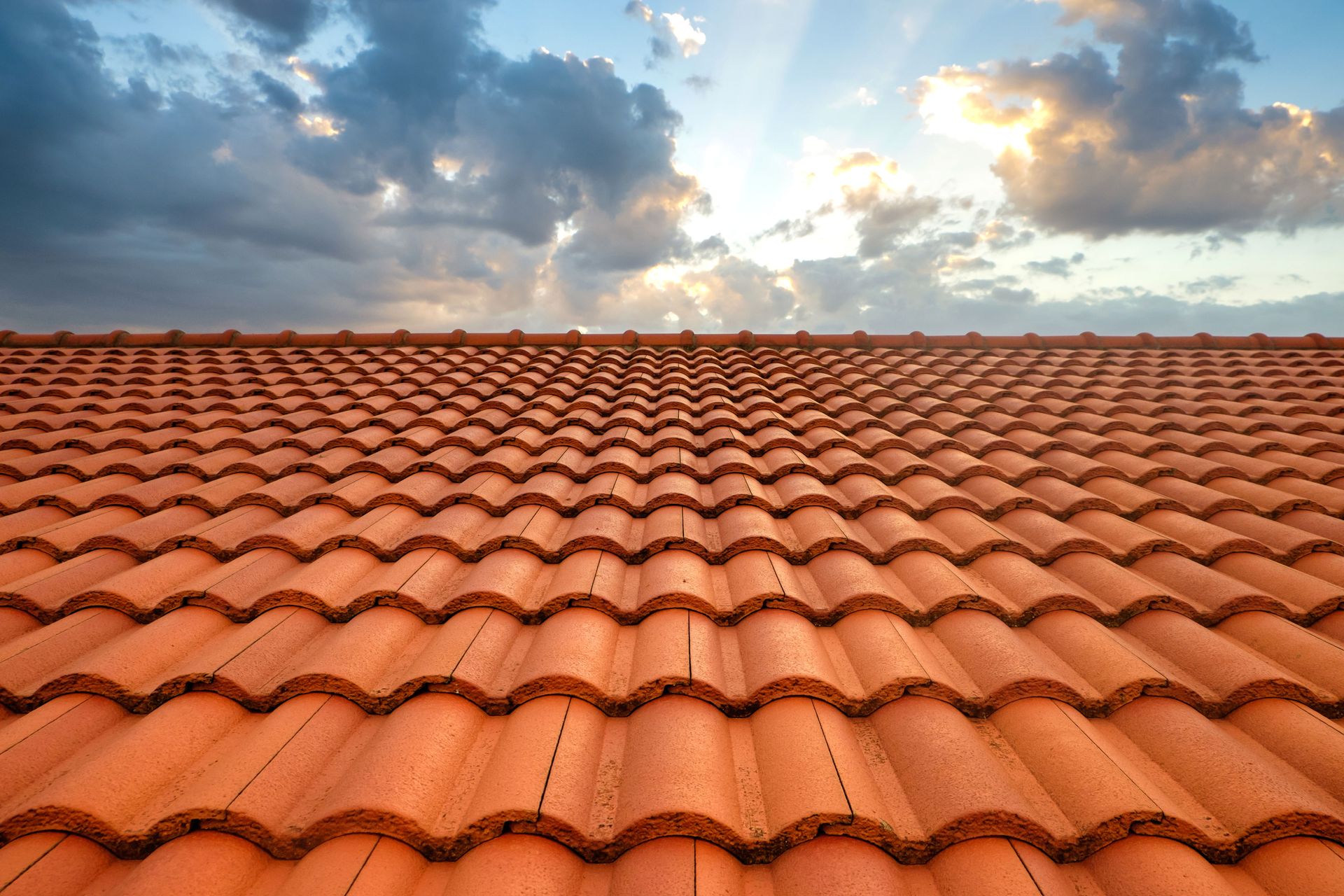 Orange tiled roof against a cloudy blue sky with the sun peeking through.