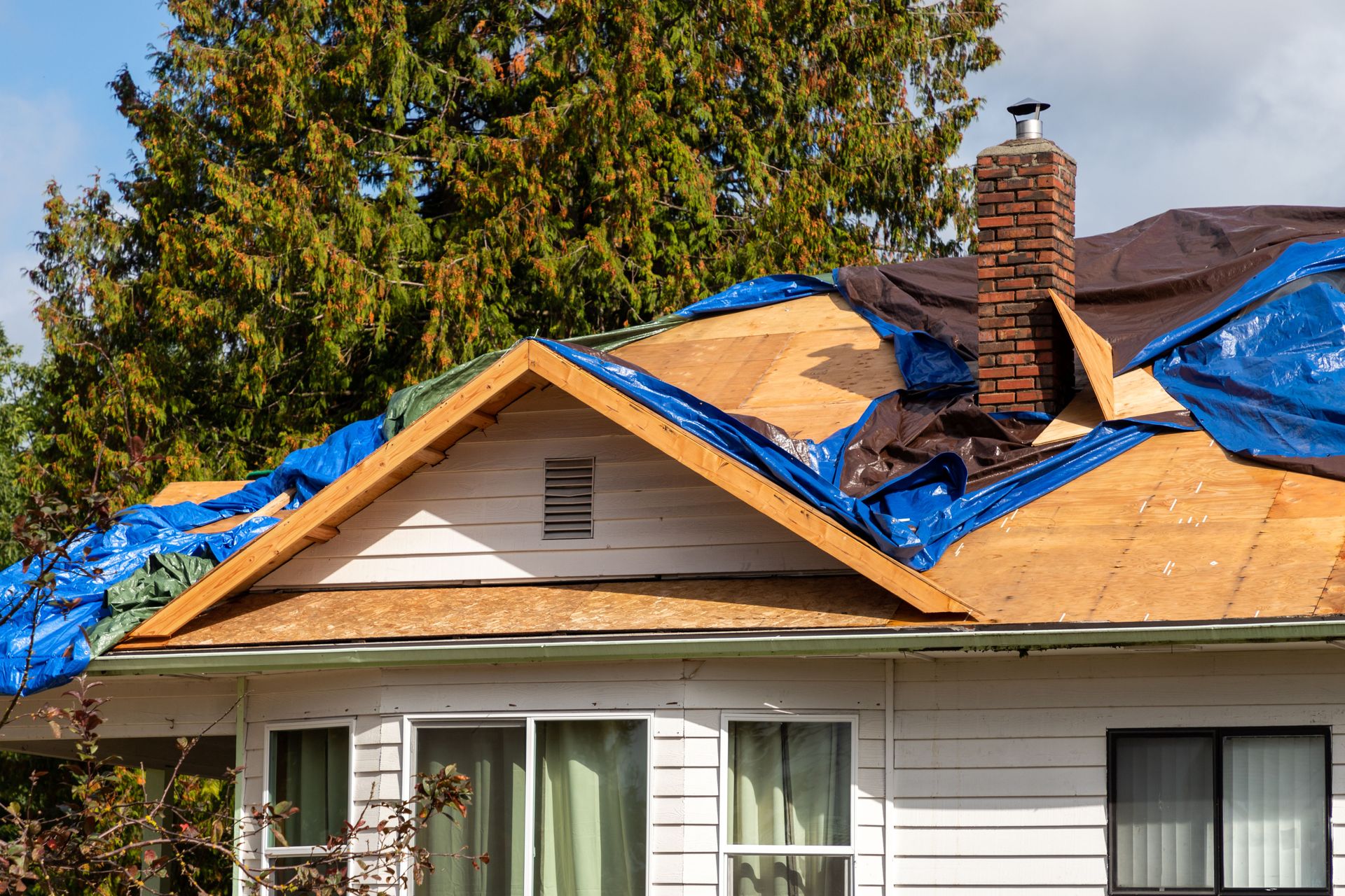 House with damaged roof covered in blue tarps, under a sunny sky.