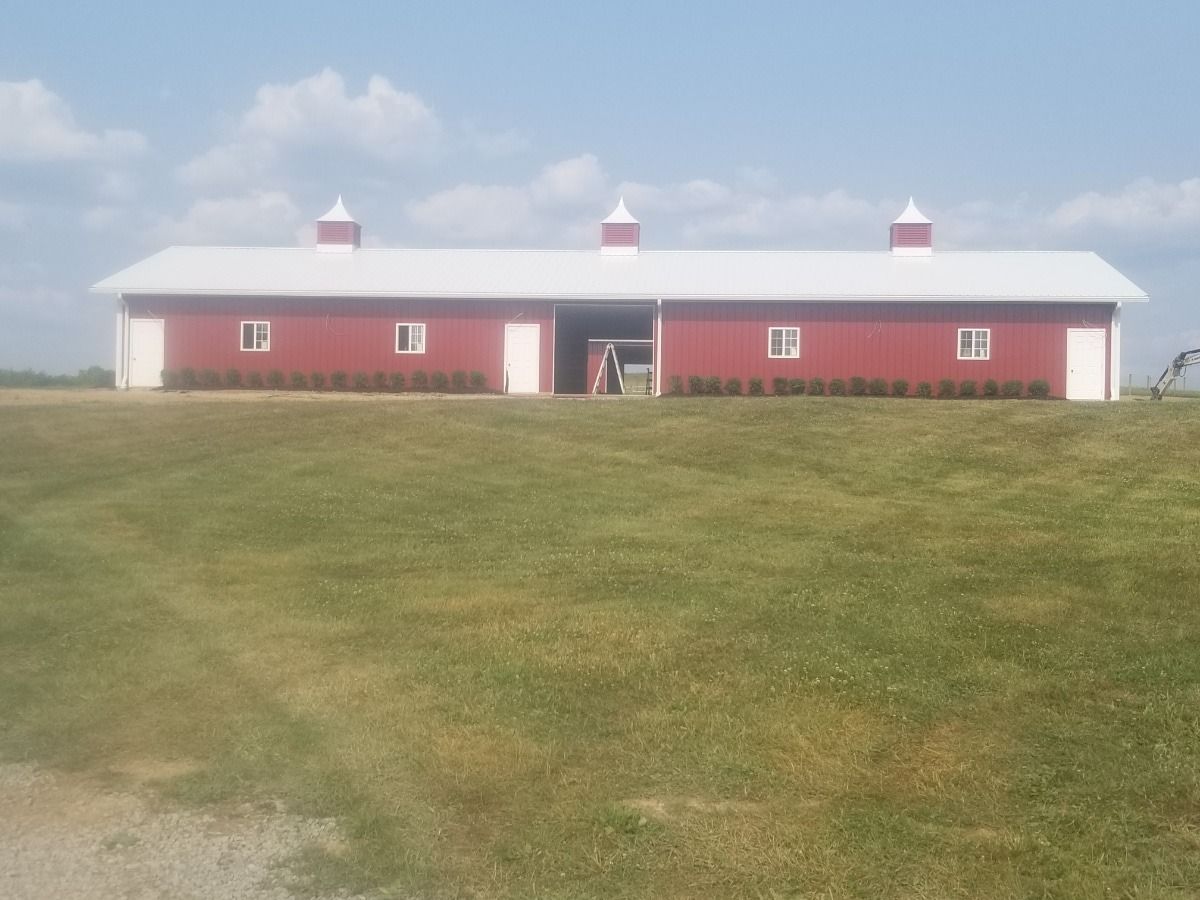 Red barn with white roof and trim on a grassy hill under a blue sky