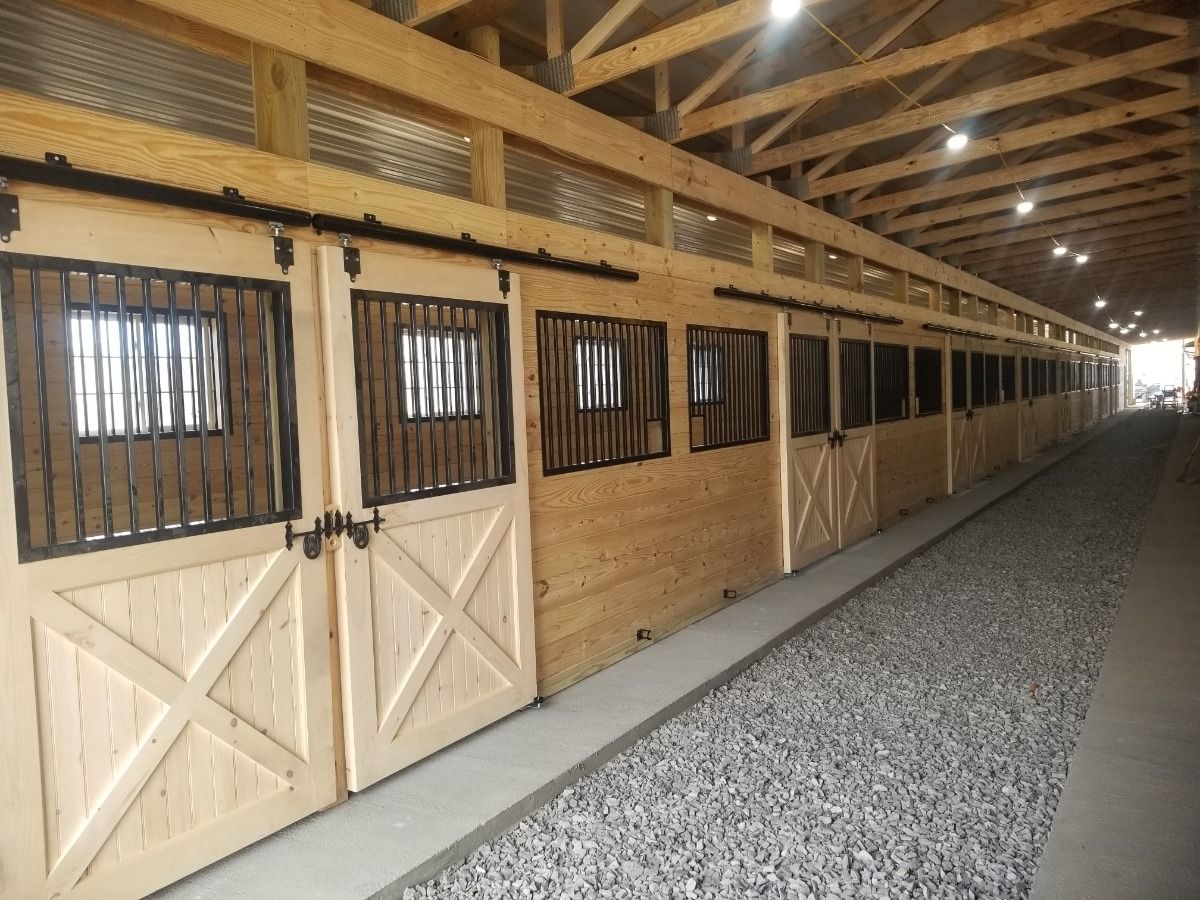 Long horse stable aisle with wooden stalls, barred windows, and gravel floor