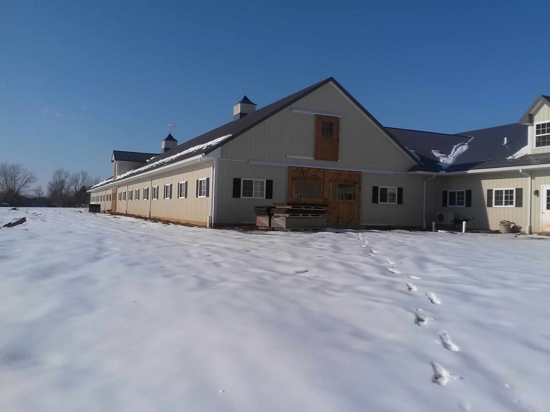 Snow-covered house with footprints leading to the front door under a clear blue sky