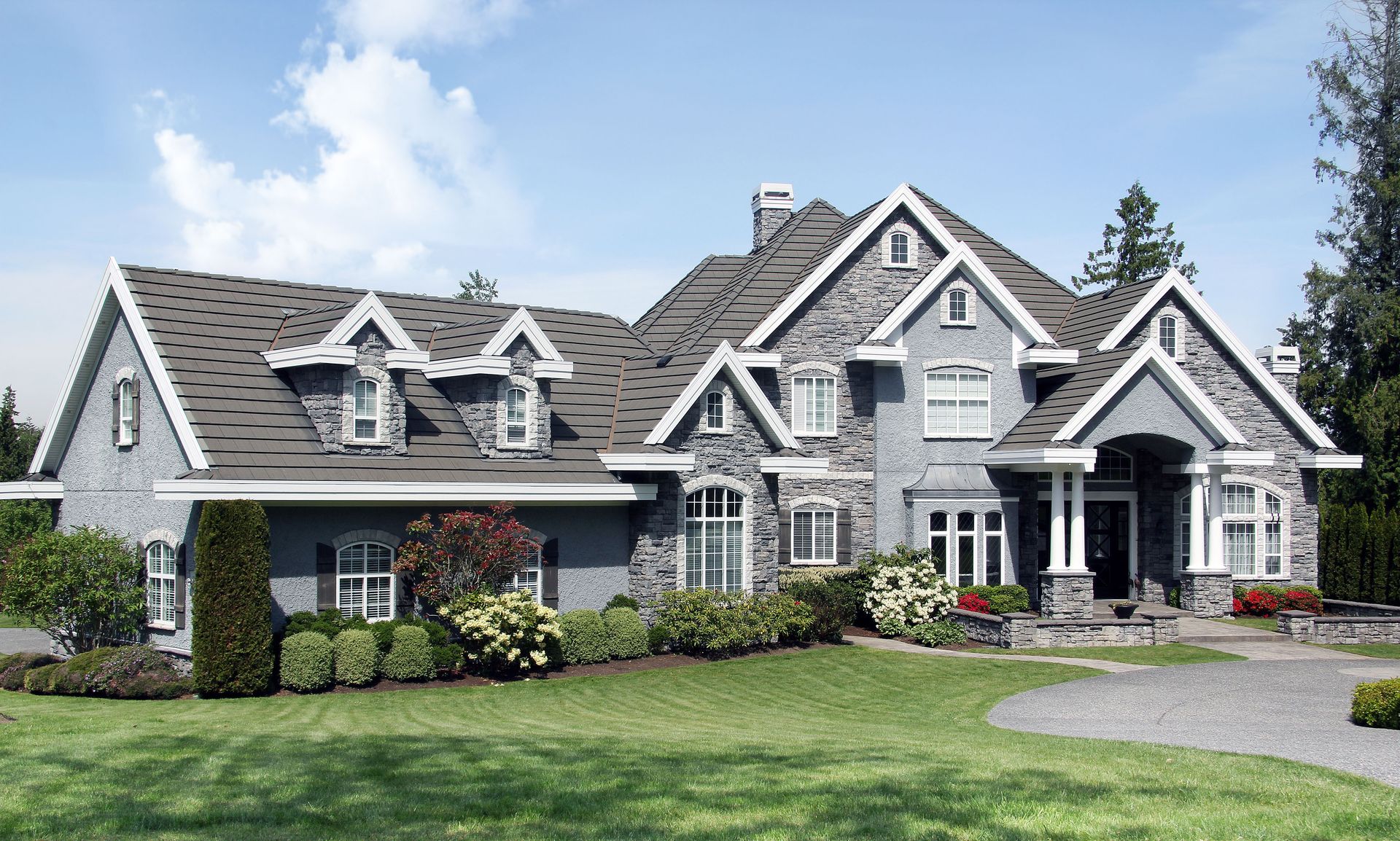 Large gray stone house with a gabled roof, white trim, and a manicured front lawn