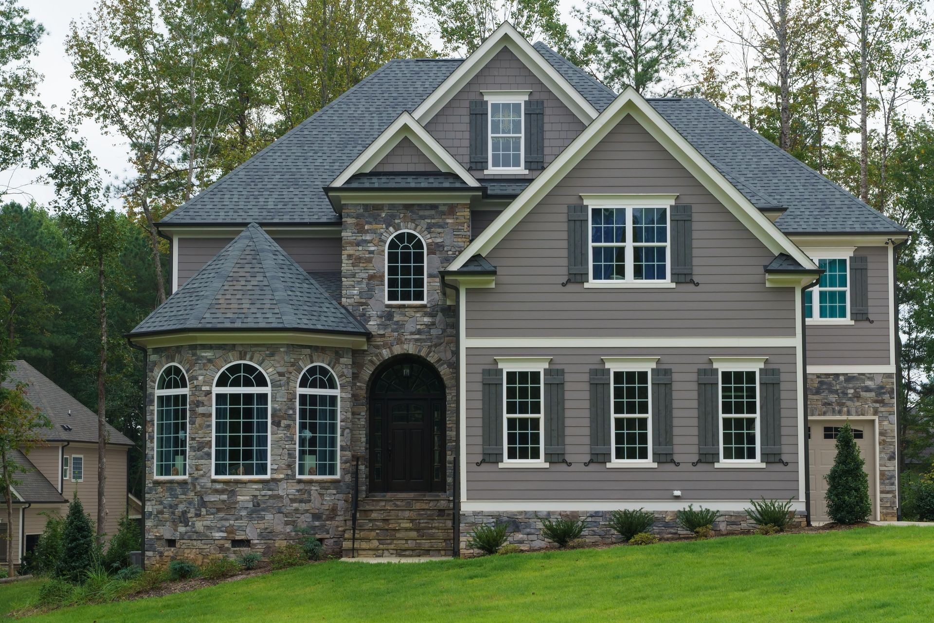 Large two-story suburban house with gray siding, stone accents, arched windows, and a green lawn