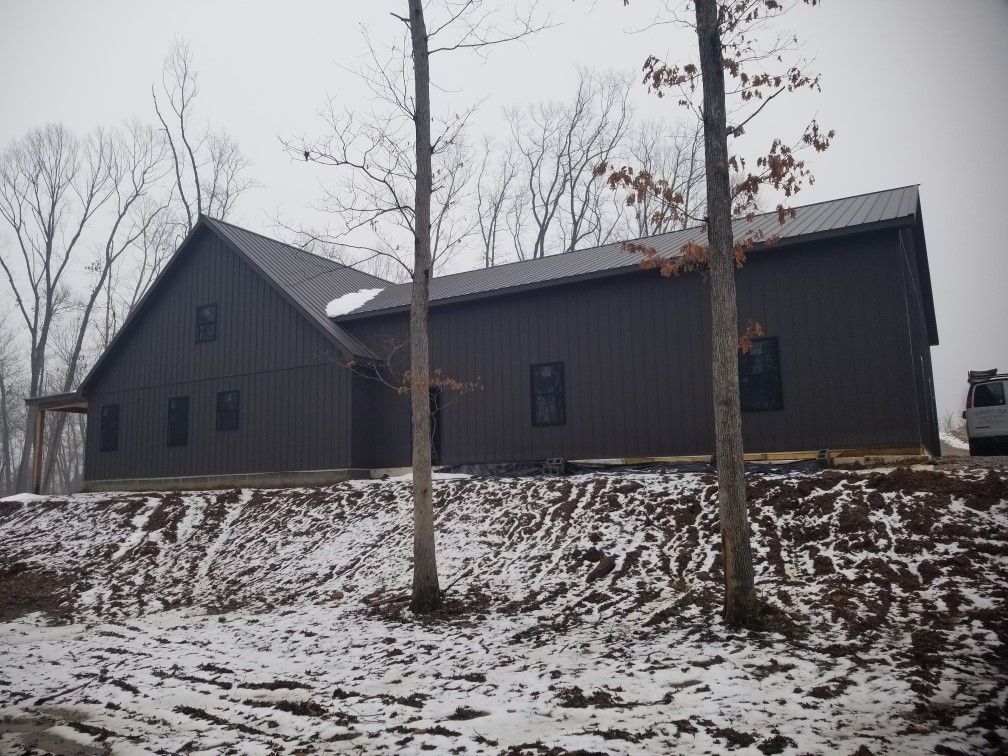 Dark house with snow-dusted yard and leafless trees on a winter day