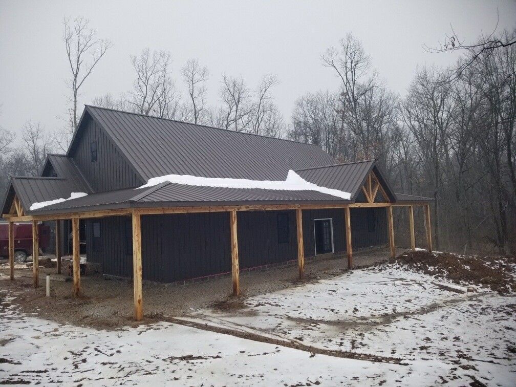 Snow-dusted wooden house under construction in a leafless wooded area