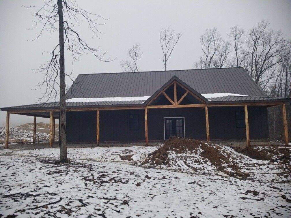 Snow-dusted unfinished house with dark roof and wooden porch on a foggy, barren lot