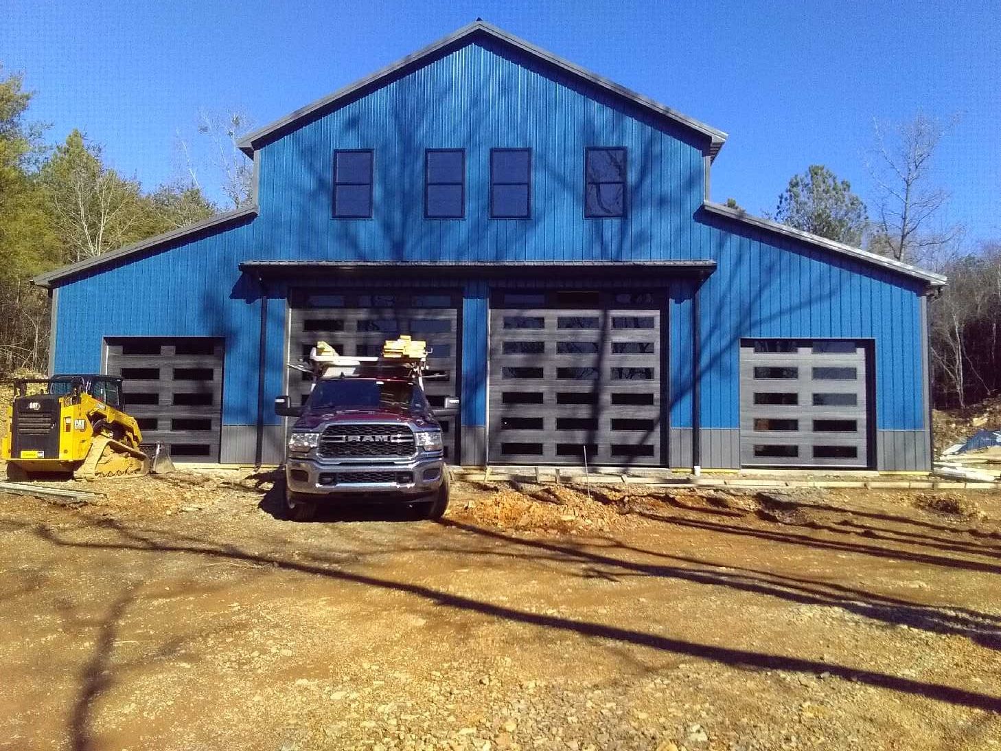 Blue metal barn with garage doors, a truck parked in front, and a yellow vehicle on the left.