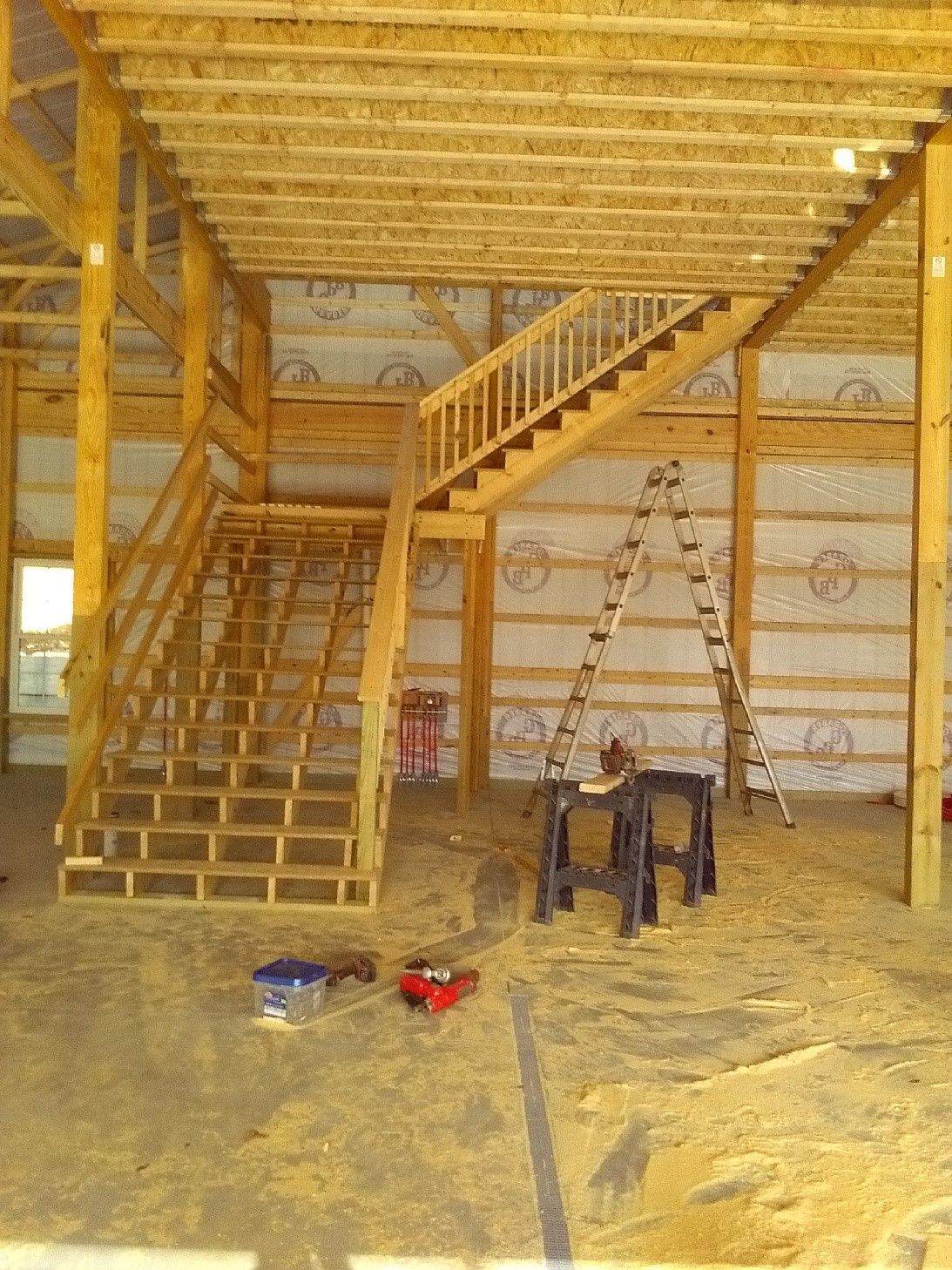 Unfinished wooden interior with stairs, ladder, and construction tools on the floor