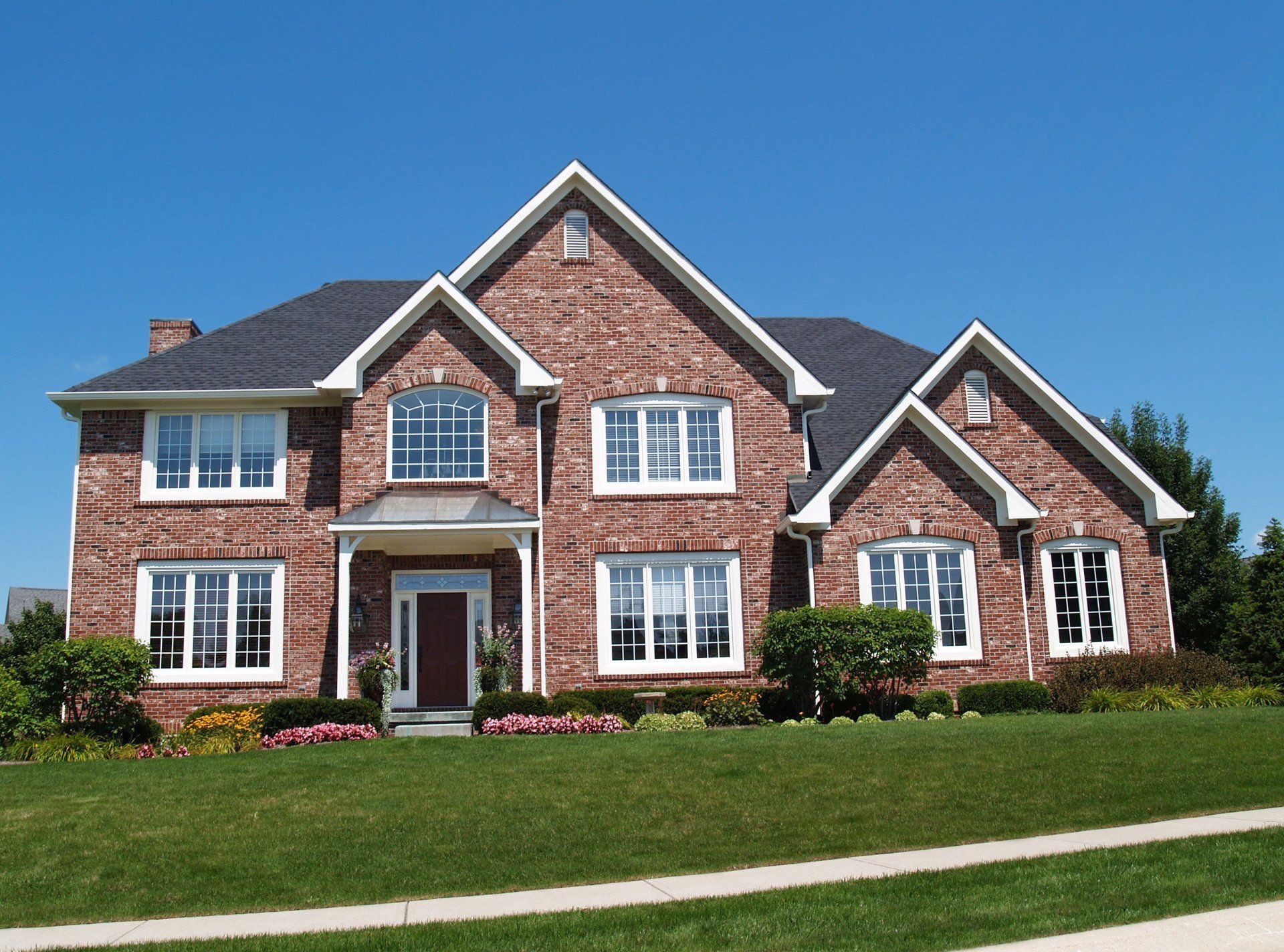 Large two-story brick house with white trim and a manicured lawn under a clear blue sky