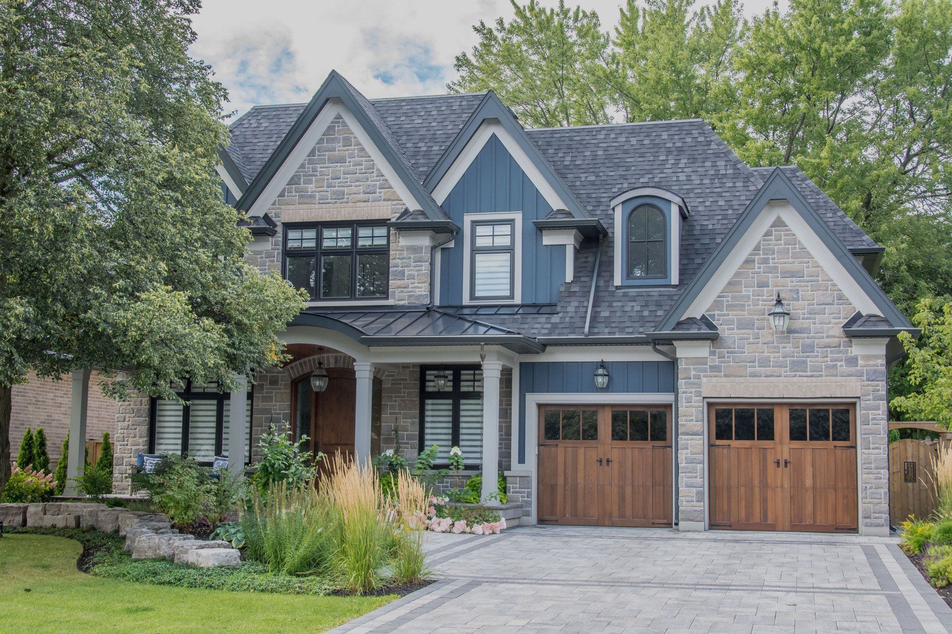 Two-story suburban house with gray siding, stone accents, and a two-car garage at the end of a driveway