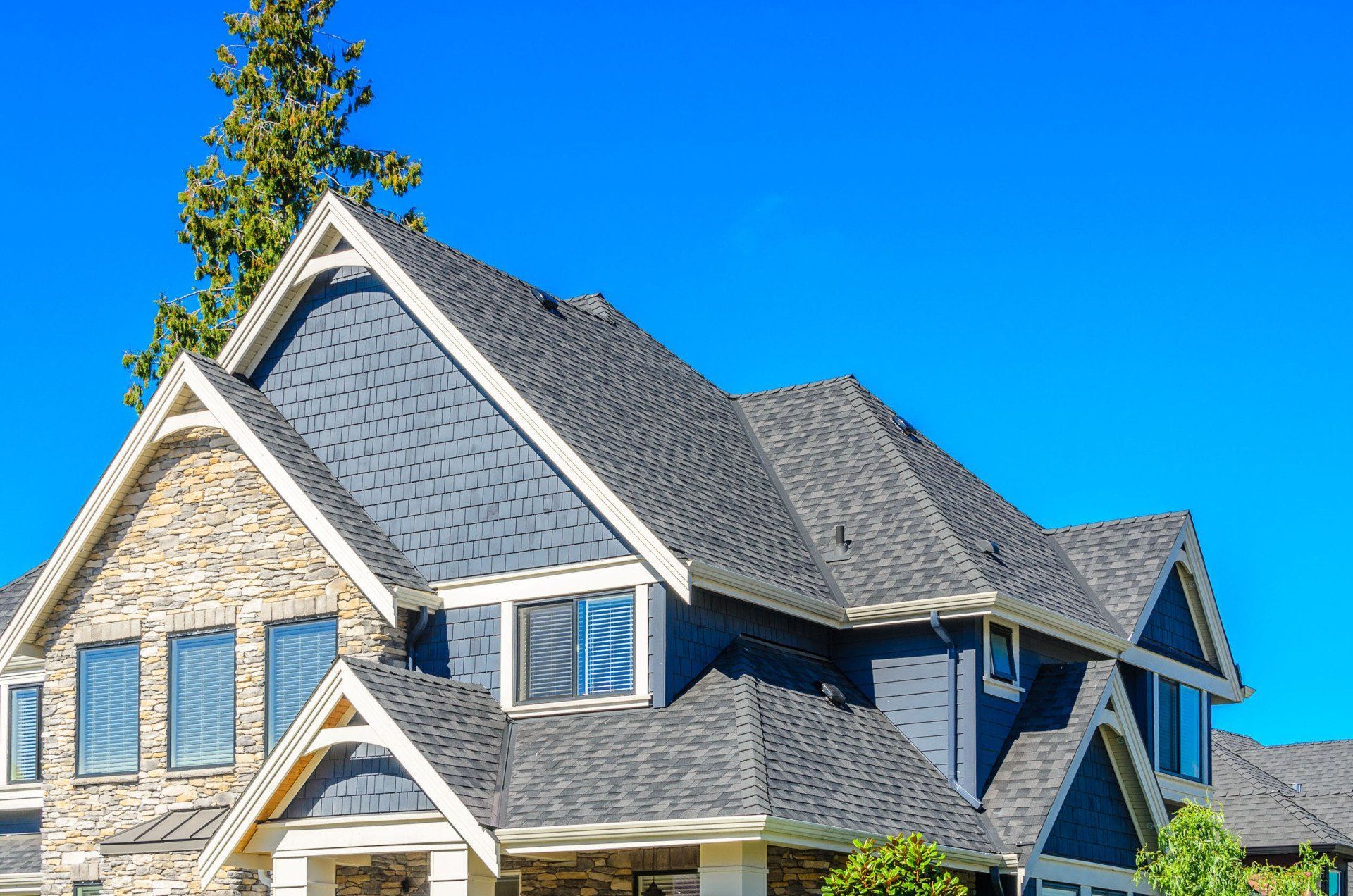 Large gray suburban house with gabled roof and blue shutters under a bright blue sky