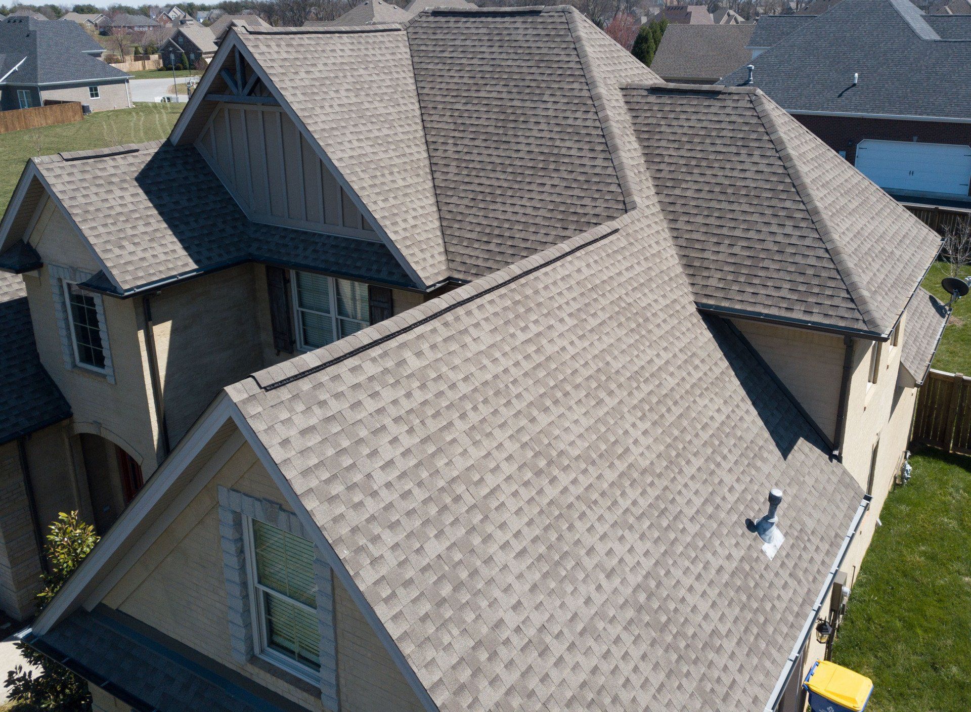 Aerial view of a gray-shingled suburban house roof with multiple gables and skylights.