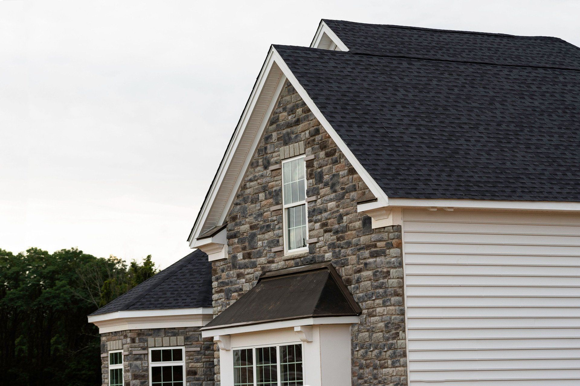 Stone house exterior with white siding and dark shingled roof under a cloudy sky