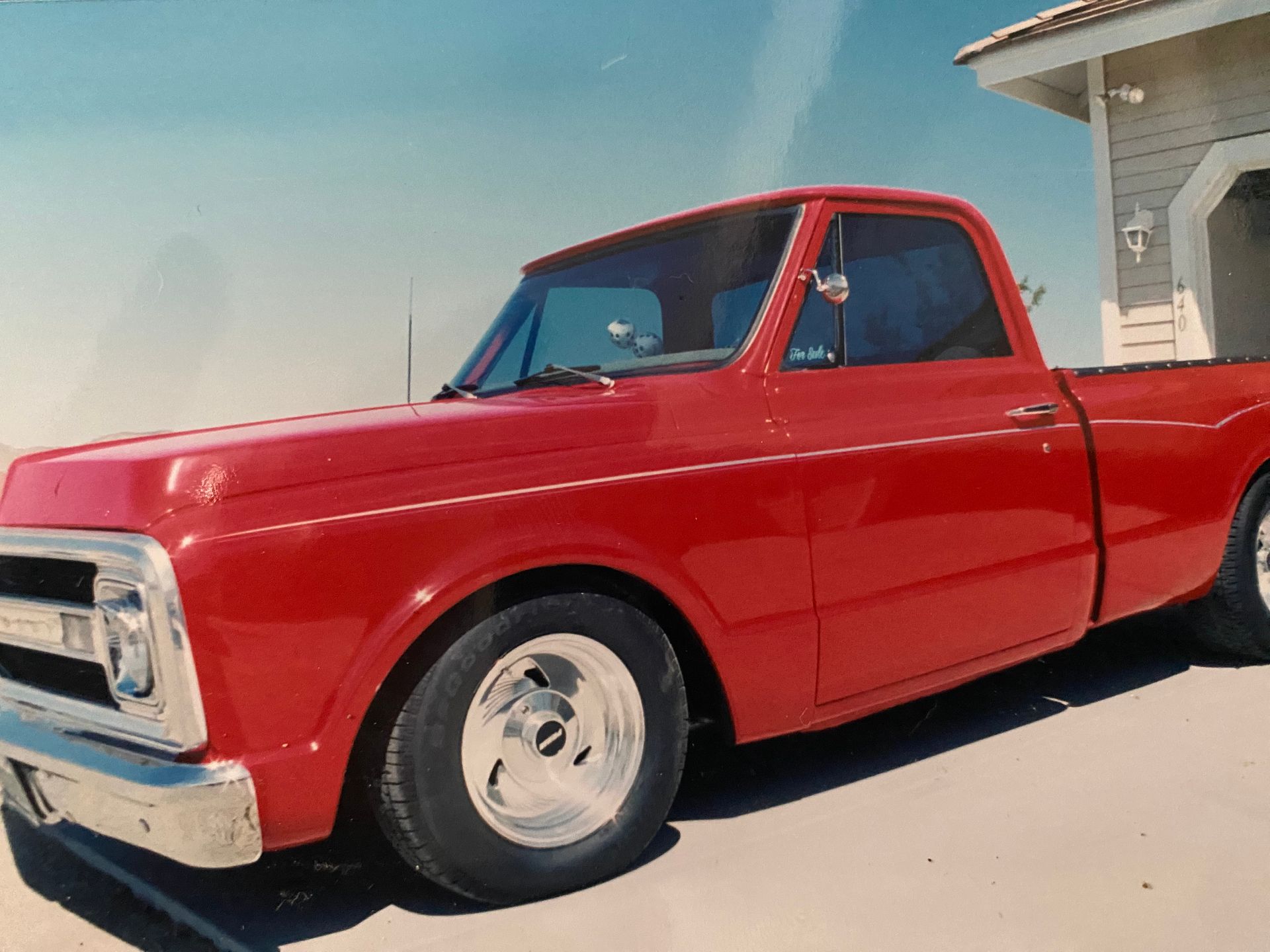 Red classic Chevrolet pickup truck parked in front of a house on a sunny day.