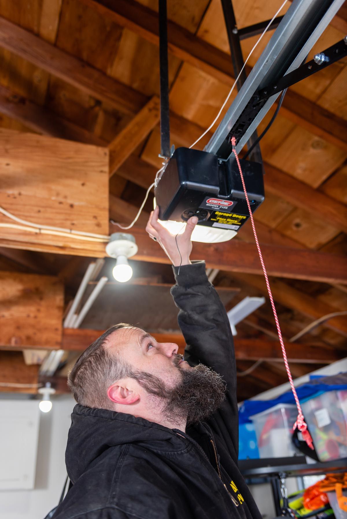 A man is fixing a garage door opener in a garage.