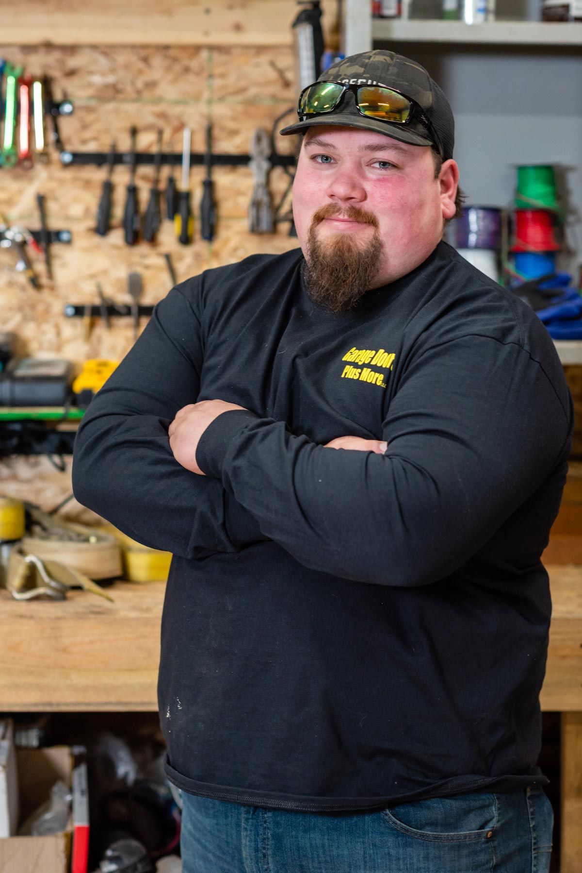 A man with a beard is standing in front of a workbench with his arms crossed.