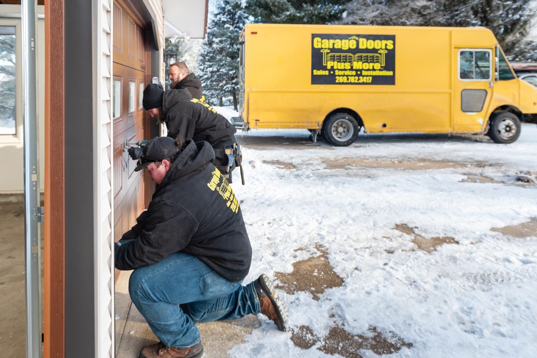 Two men are working on a garage door next to a yellow garage doors truck.