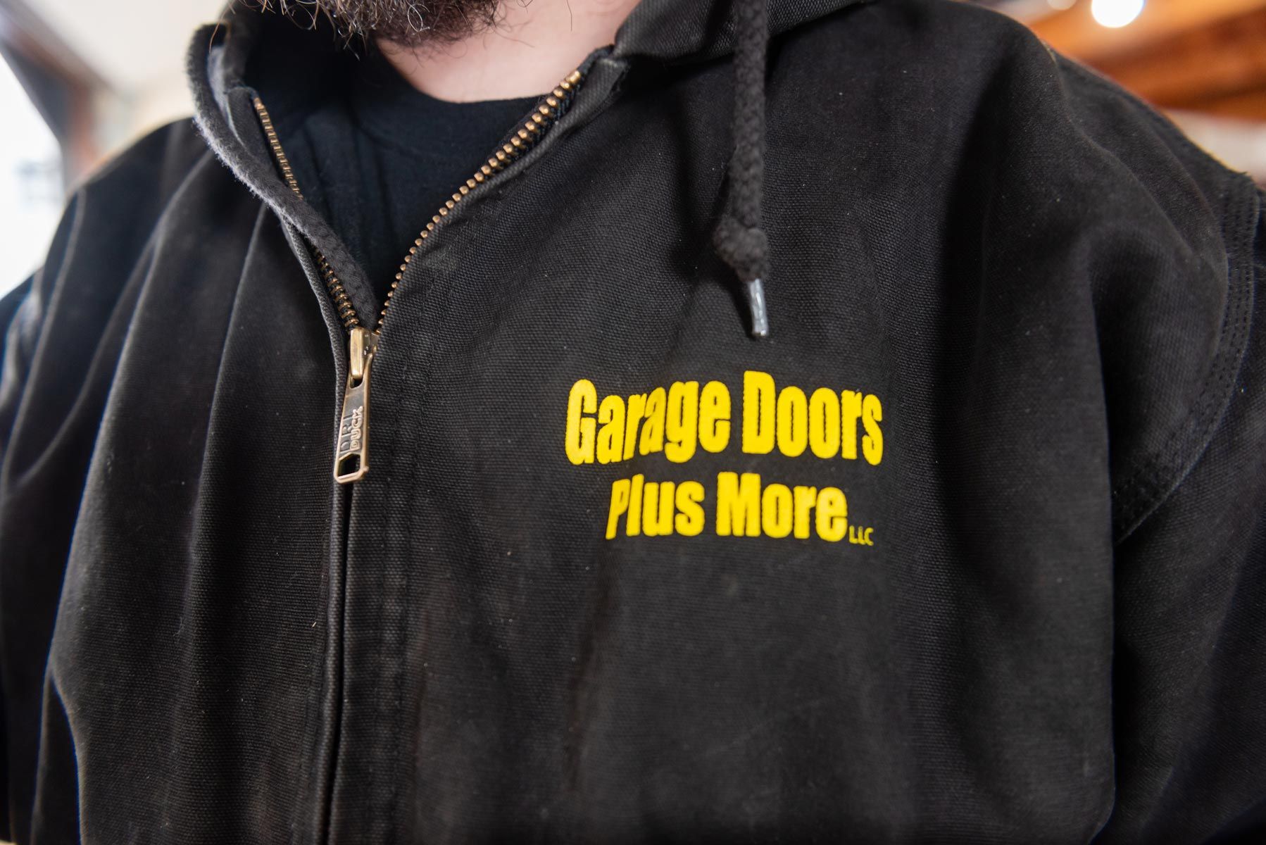 A man wearing a black hoodie that says garage doors plus more