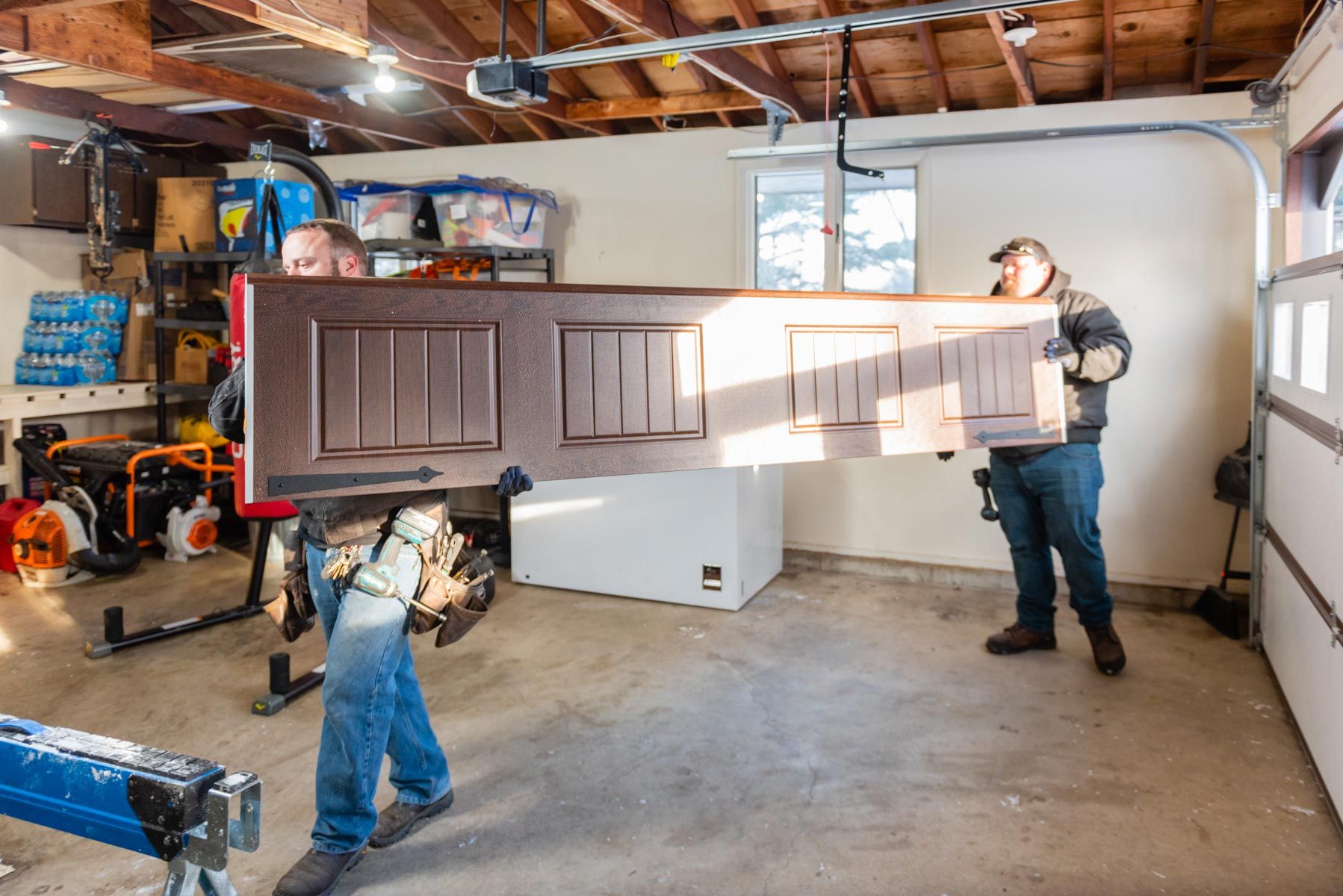 Two men are carrying a door in a garage.
