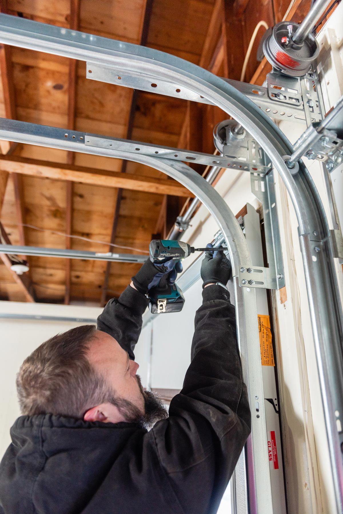 A man is fixing a garage door with a drill.