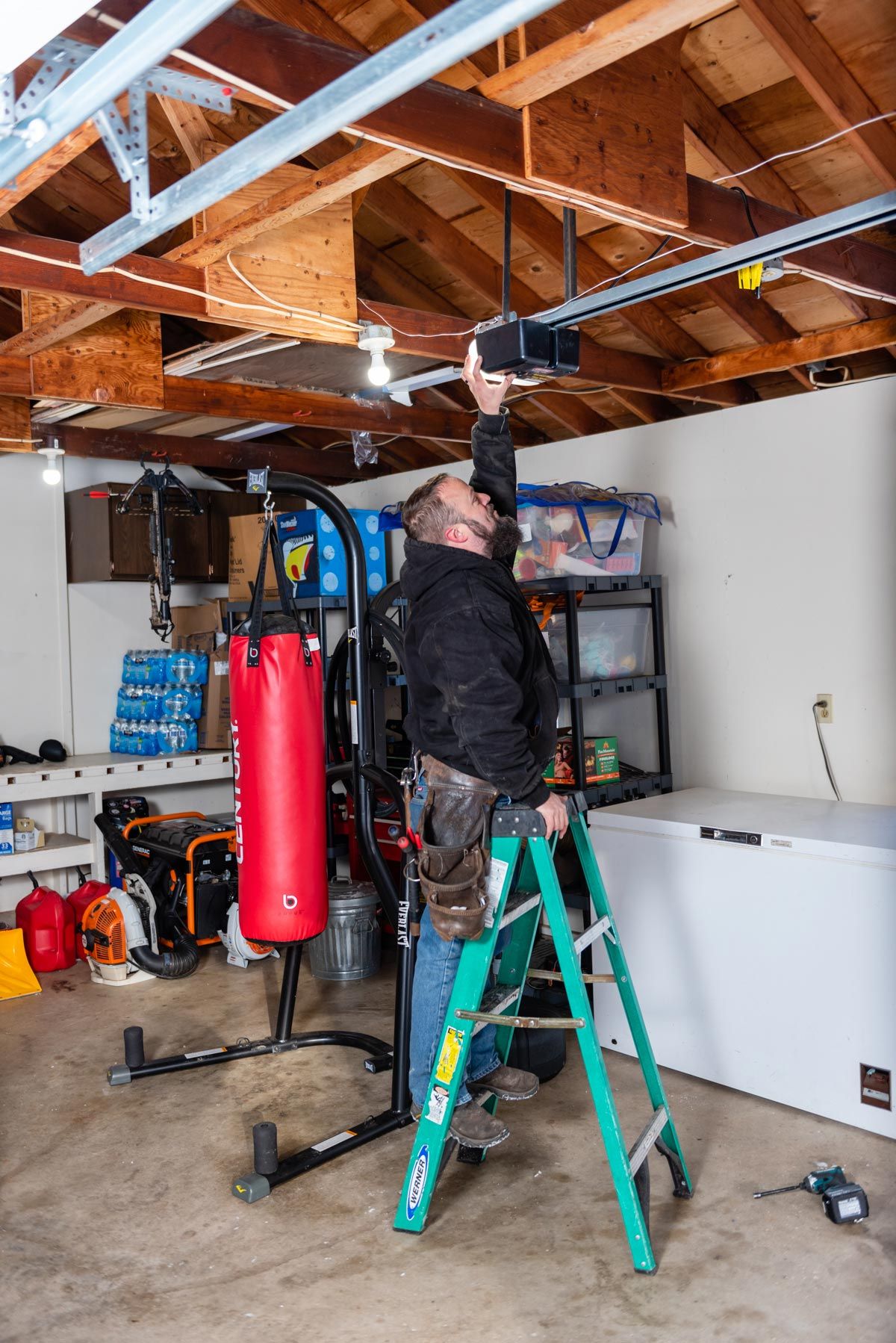 A man is standing on a ladder in a garage working on a garage door opener.