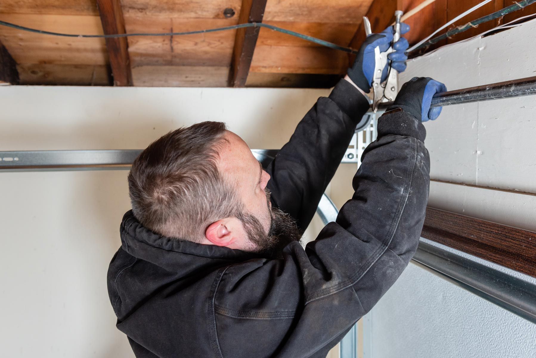 A man is working on a garage door with a pair of pliers.