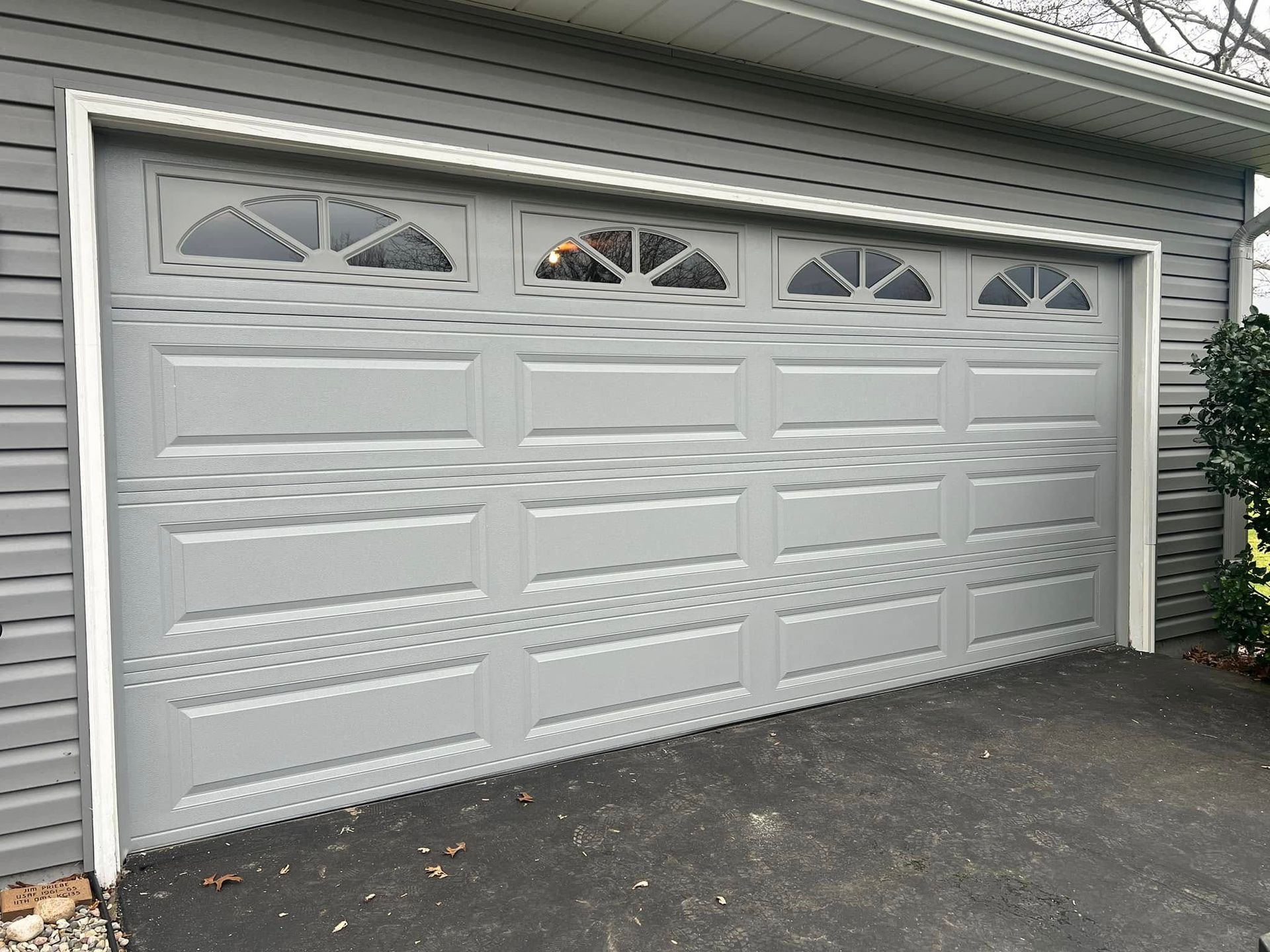 A gray garage door with a white trim is sitting on the side of a house.