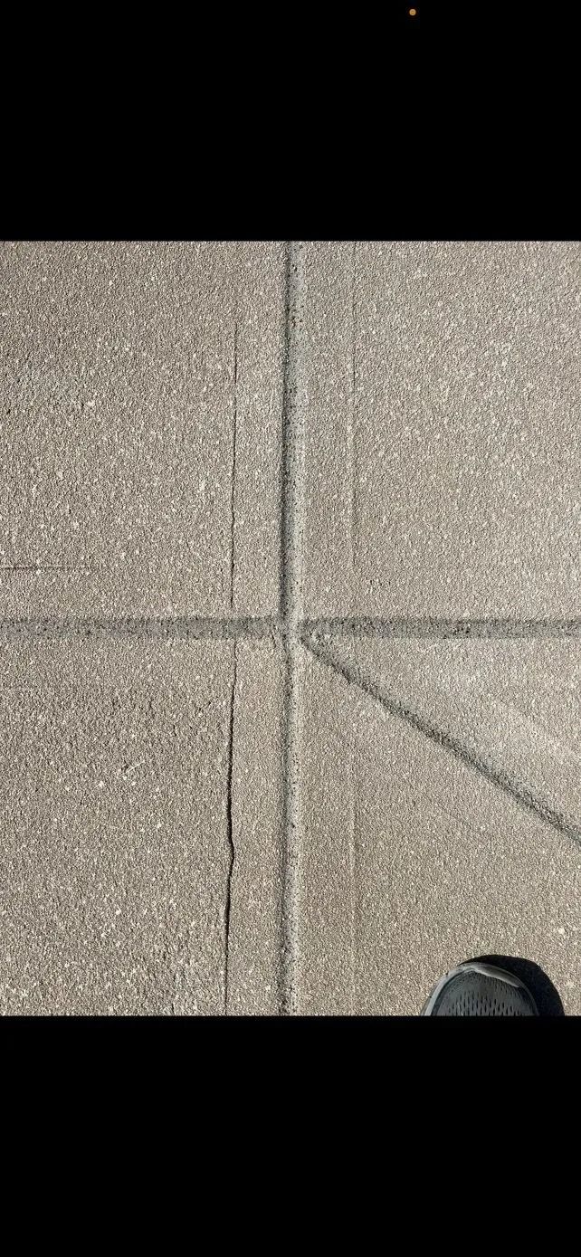 Cracked pavement with dark lines forming a cross shape. A foot is visible at the bottom.
