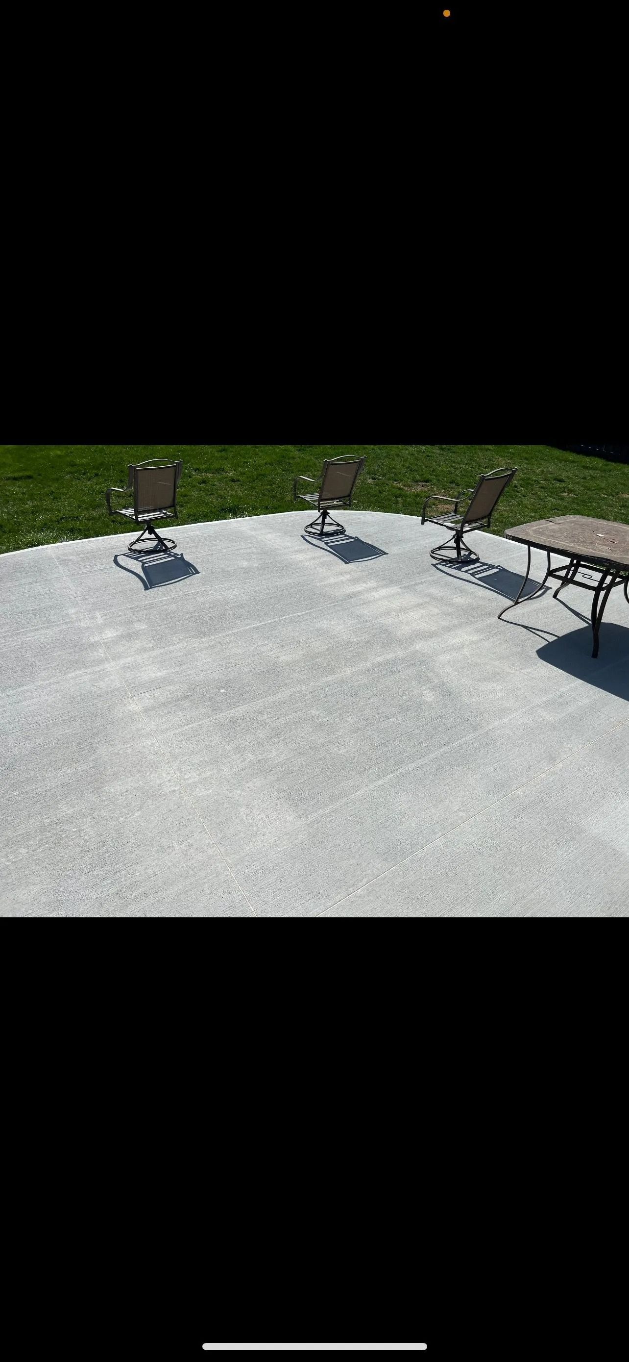 A sunny outdoor patio with three chairs and a table on a concrete surface. Green grass in the background.